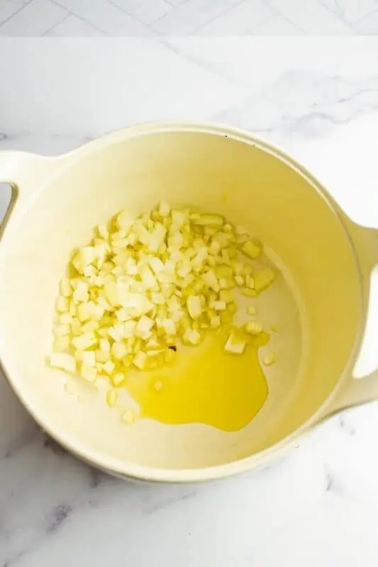 White onions cooking in olive oil in a large white pot.