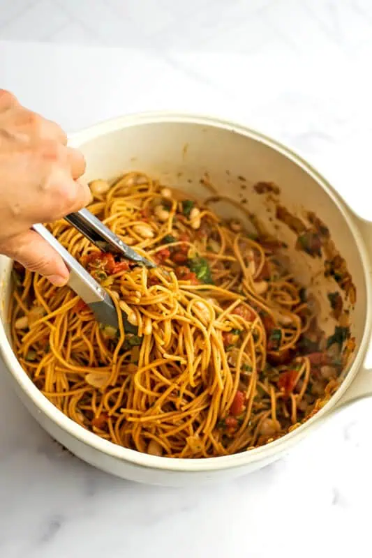 Tongs tossing the pasta in with the tomato mixture.