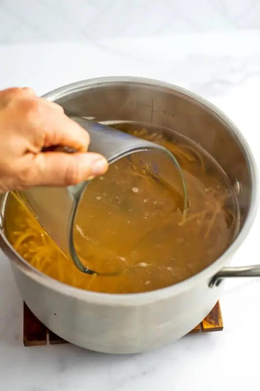 Hang holding a glass measuring cup that is collecting some of the cooking liquid from the pasta.