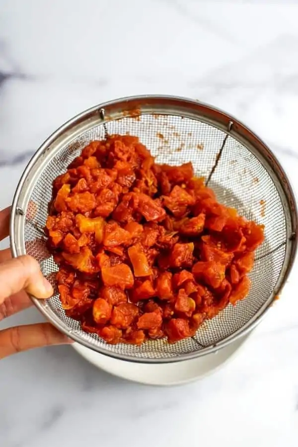 Canned diced tomatoes in mesh strainer.