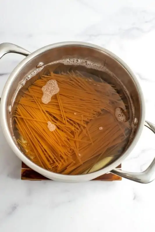 Pasta being added to boiling water in stainless steel pot.