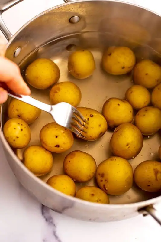 Fork piercing baby potatoes in water to check if they are done.