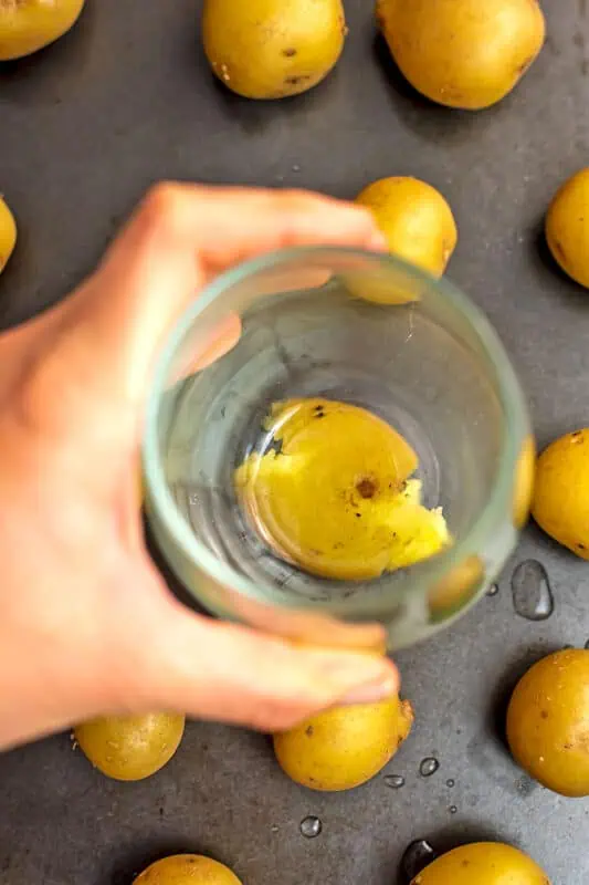 Hand holding glass, smashing cooked potatoes.