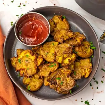 Air fryer smashed potatoes on grey plate with ramekin of ketchup.