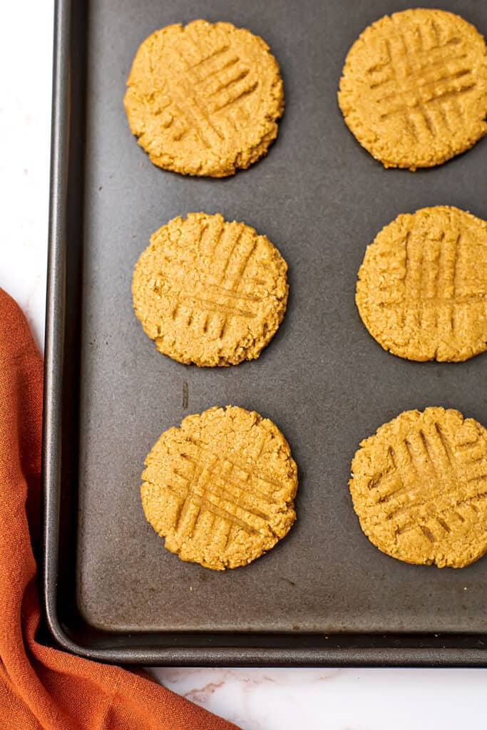 Six peanut butter almond flour cookies on a sheet pan.