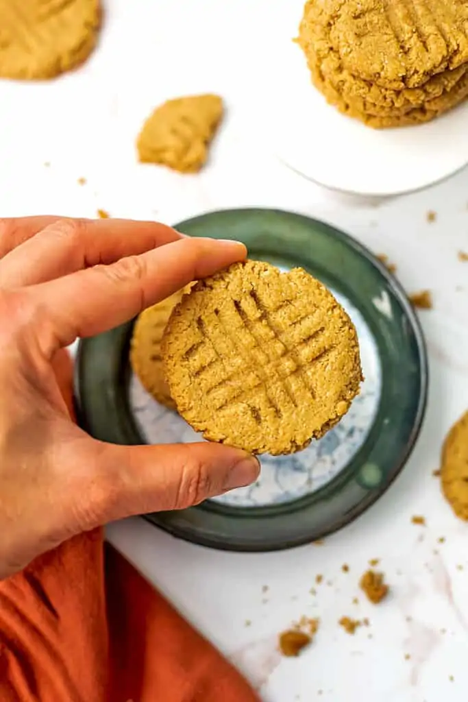 Hand picking up a gluten free peanut butter cookie from a green rimmed plate.