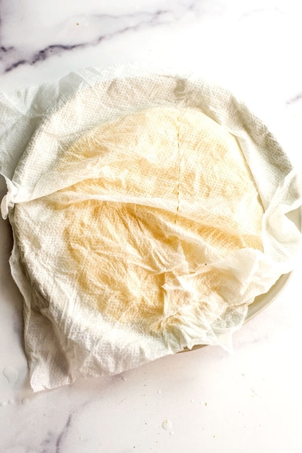 Wet paper towel over plate filled with tortillas.
