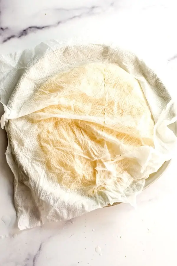 Wet paper towel over plate filled with tortillas.