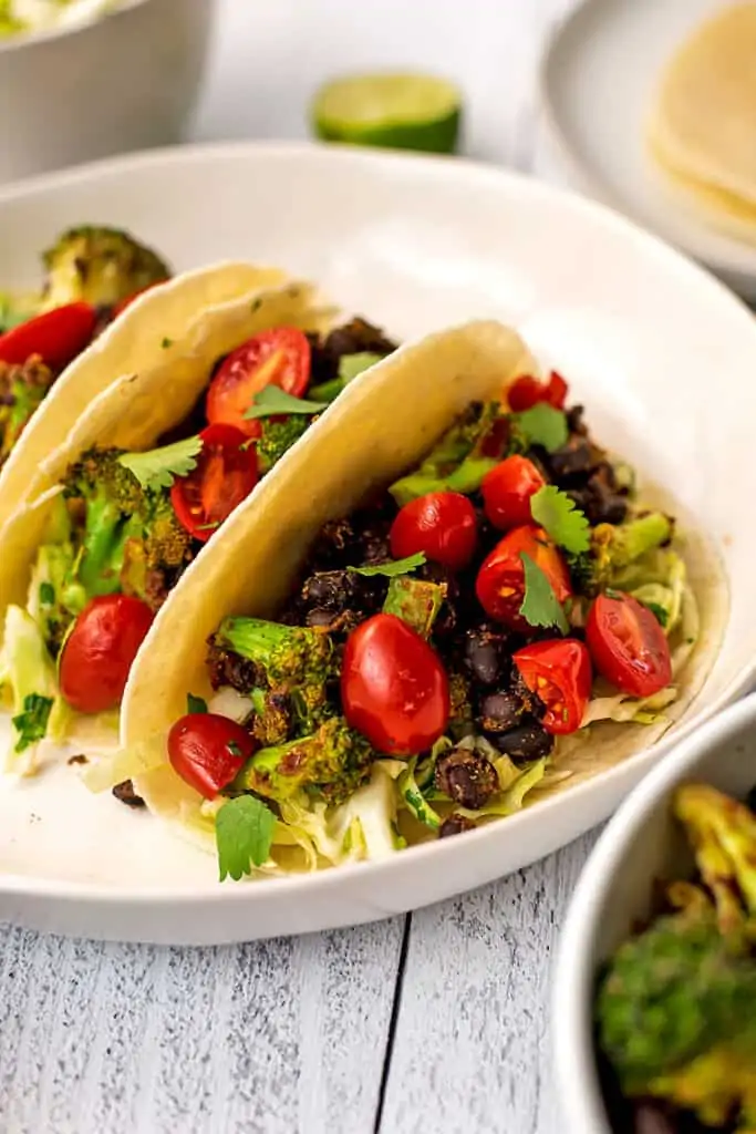 Three black bean broccoli tacos on a large white plate.