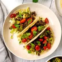 Three broccoli tacos on a large white plate.
