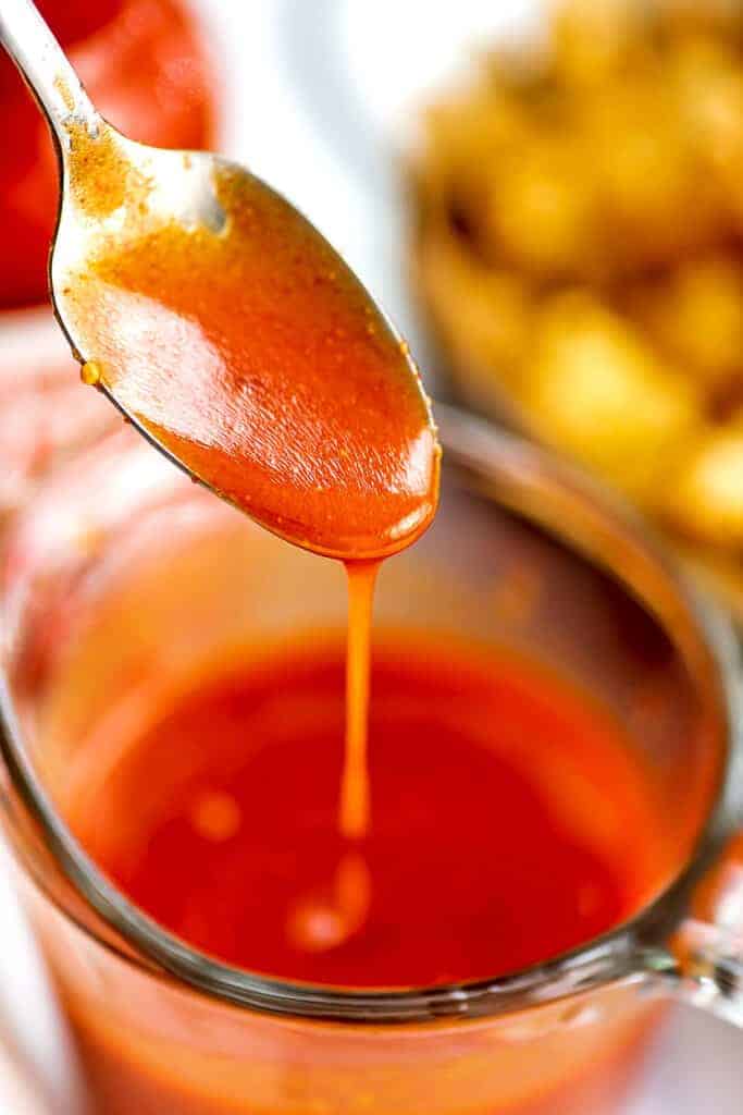 Spoon pouring vegan buffalo sauce into a glass jar.