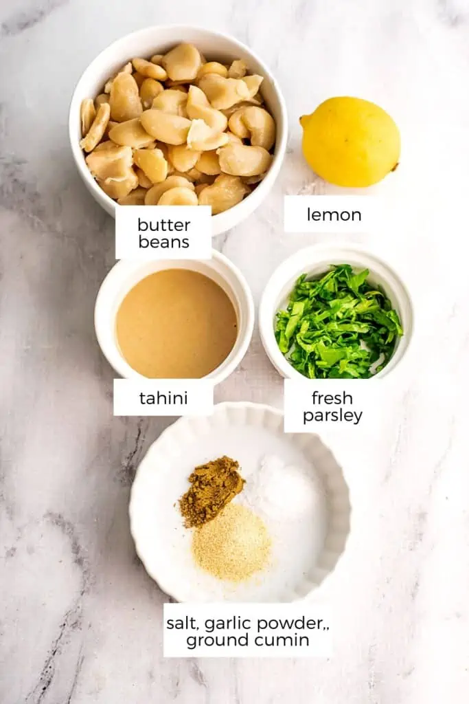 Butter bean hummus ingredients in white bowls on marble countertop.