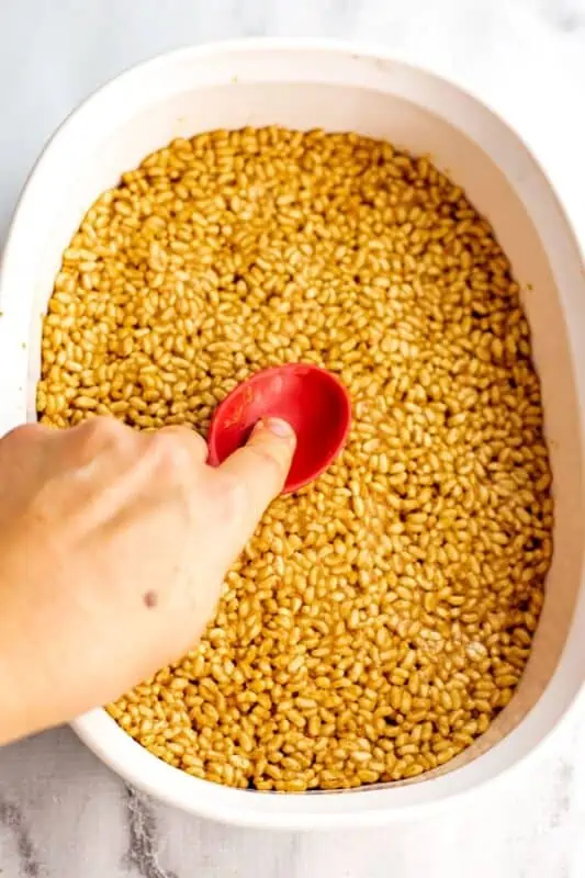 Red silicone spoon pressind down on peanut butter rice krispy mixture.