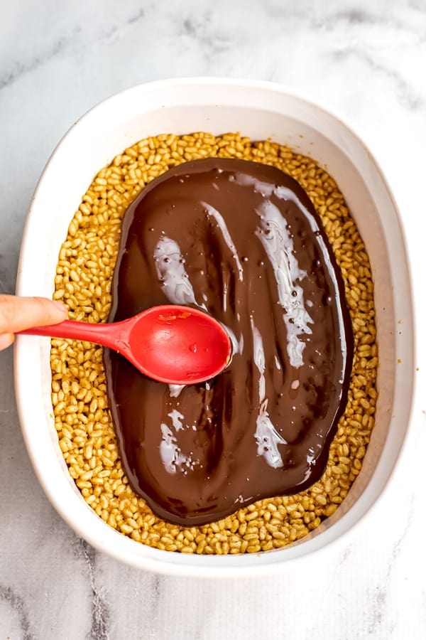 Melted chocolate being spread on top of the peanut butter rice cereal mixture.