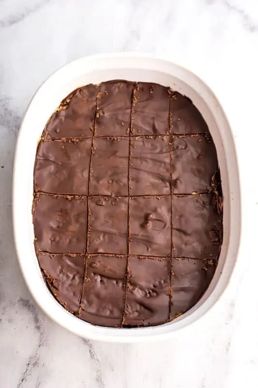 Chocolate peanut butter rice krispy treats cut into squares in a white casserole dish.