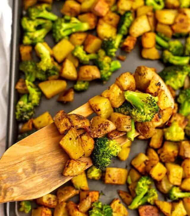 Sheet pan of roasted potatoes and broccoli with a wooden spatula.