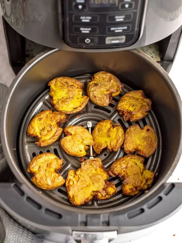 Air fryer basket filled with smashed potatoes.