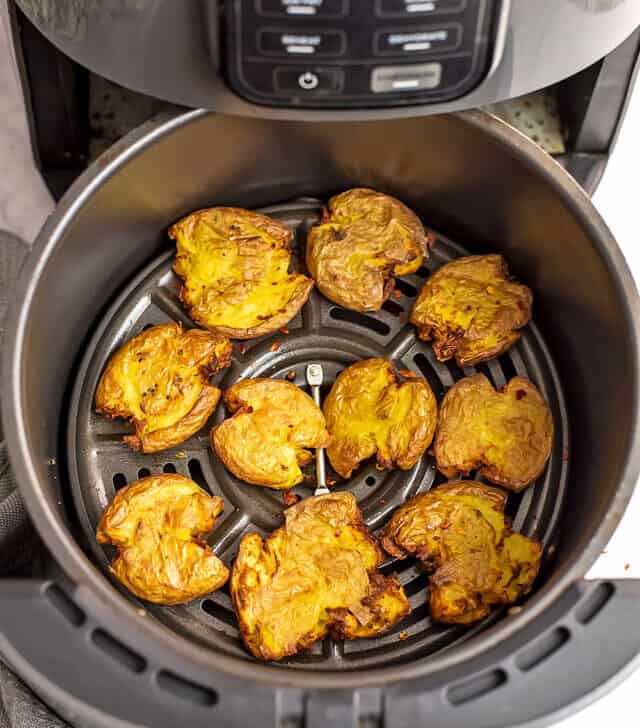 Air fryer basket filled with smashed potatoes.
