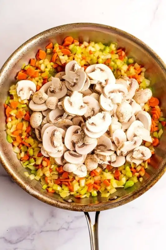 Mushrooms added to cooked veggies in stainless steel pan.