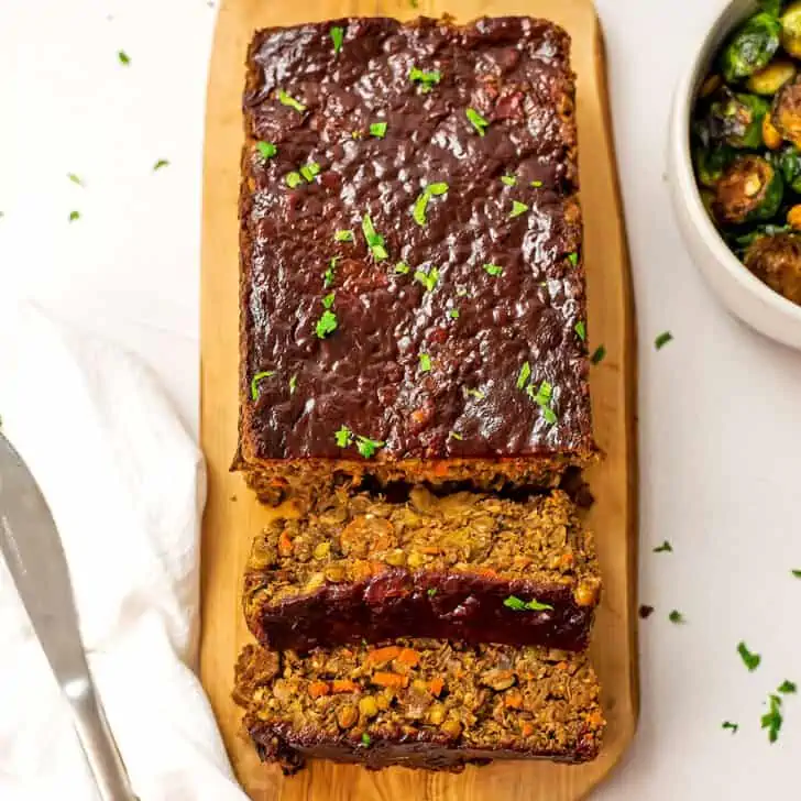 Two slices of mushroom lentil loaf being cut from the loaf on wooden cutting board.