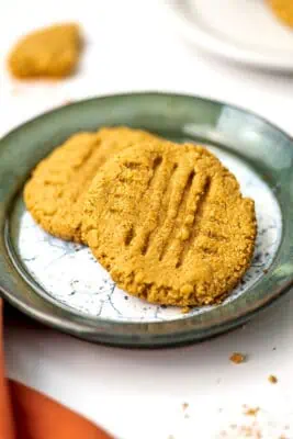 Two almond flour peanut butter cookies on a green rimmed plate.
