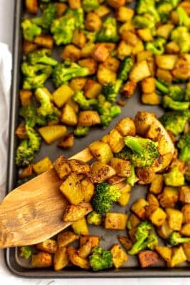 Sheet pan of roasted potatoes and broccoli with a wooden spatula.