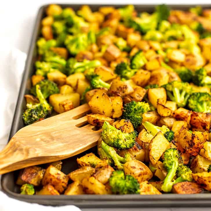 Wooden spatula in a sheet pan full of roasted potatoes and broccoli.