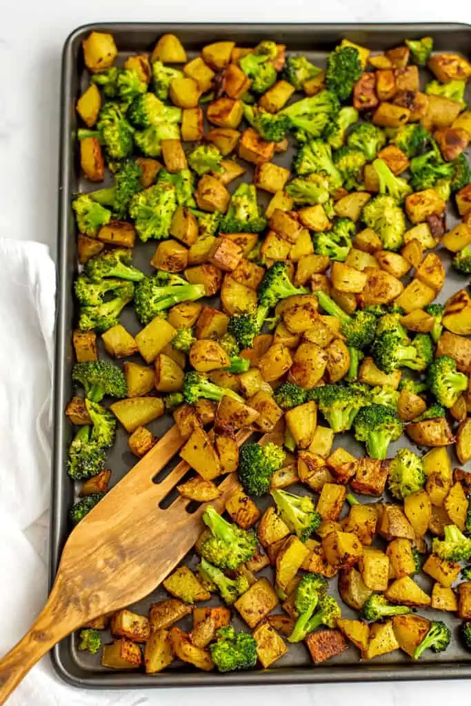 Wooden spatula in a sheet pan filled with roasted broccoli and potatoes.