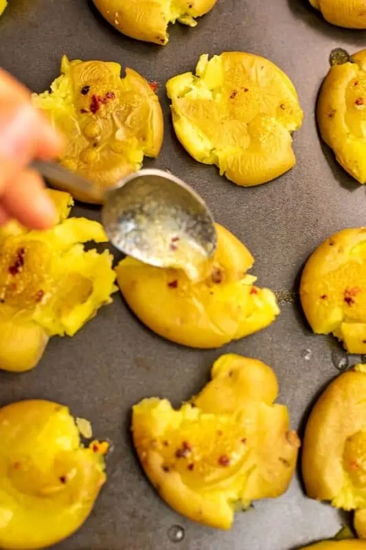 Olive oil mixture being spooned over the smashed potatoes.