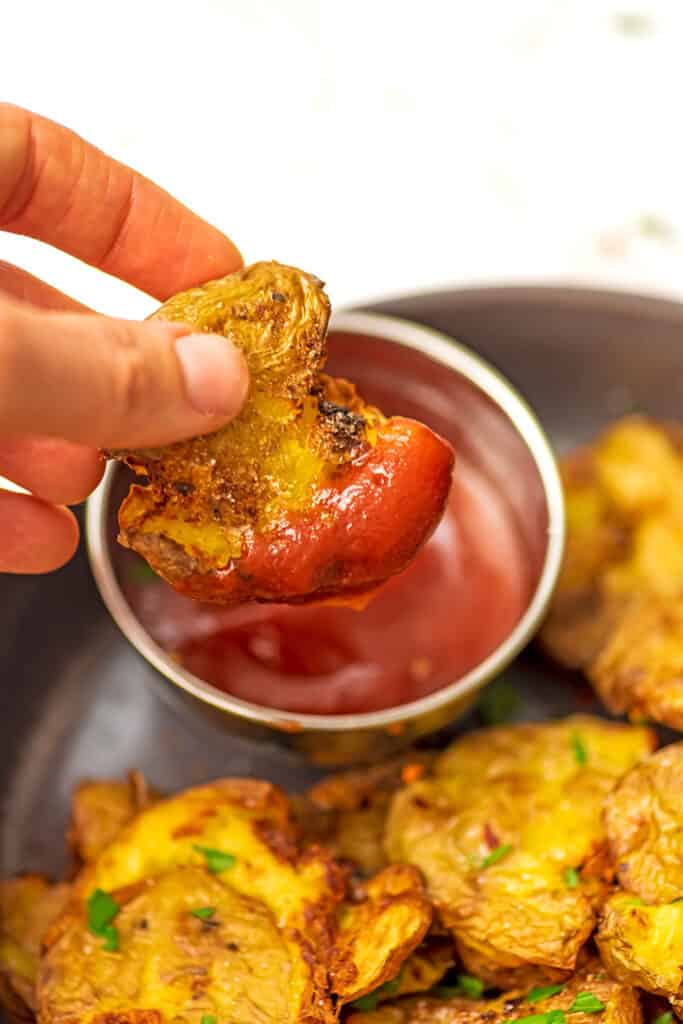 Silver ramekin filled with ketchup, a smashed potato being dipped in.