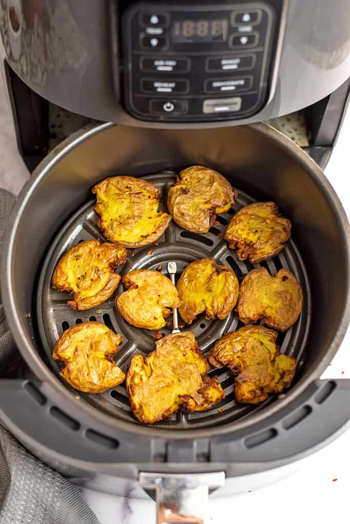 Air fryer basket filled with smashed potatoes.