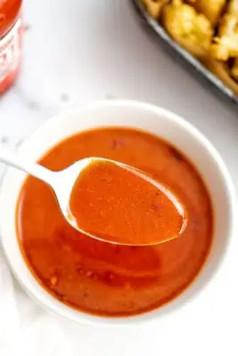 White bowl of vegan buffalo sauce, spoonful of sauce over top.