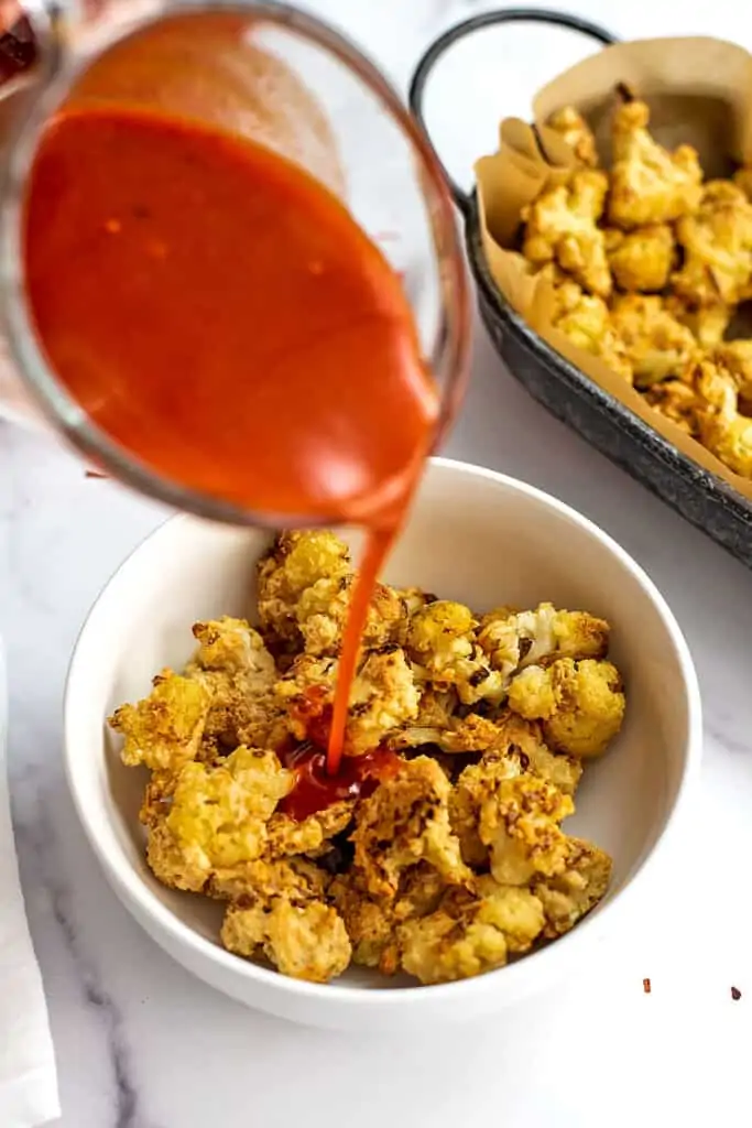 Buffalo sauce no butter being poured over cauliflower wings.