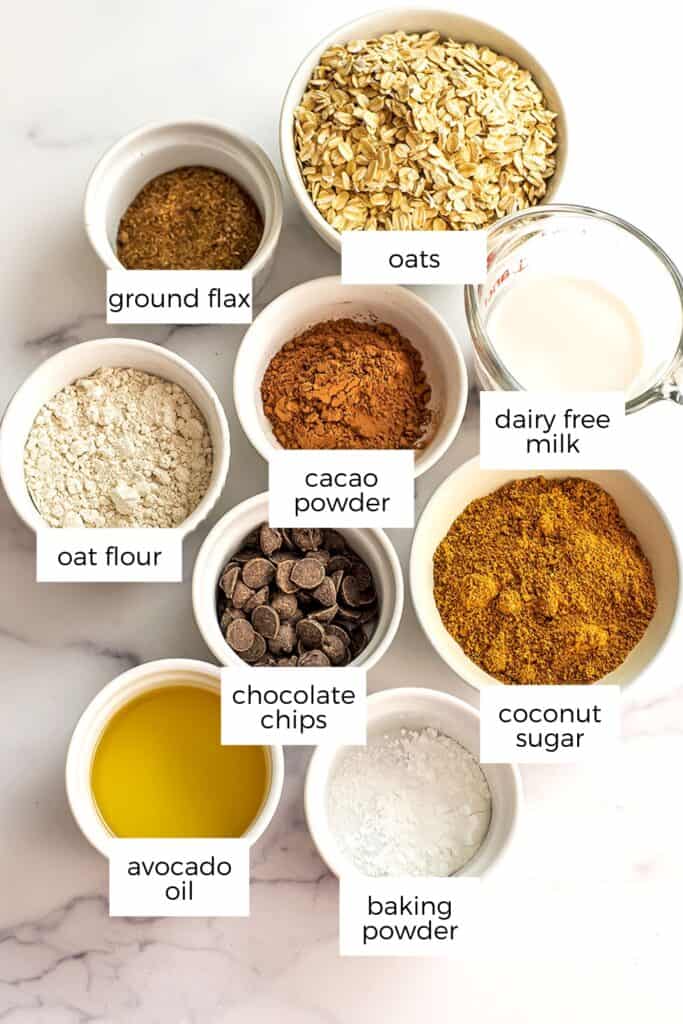 Ingredients to make chocolate oatmeal cookies in ramekins on marble countertop.