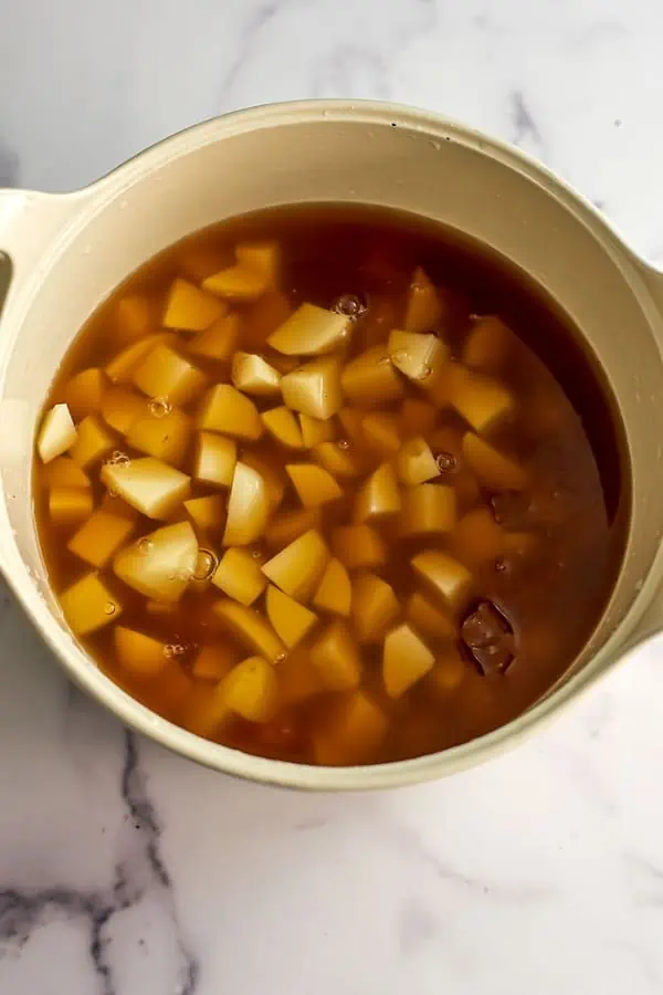 Vegetable broth with potatoes in large white pot.
