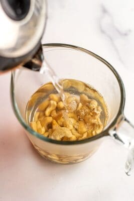 Boiling water being poured over cashews in glass measuring cup.