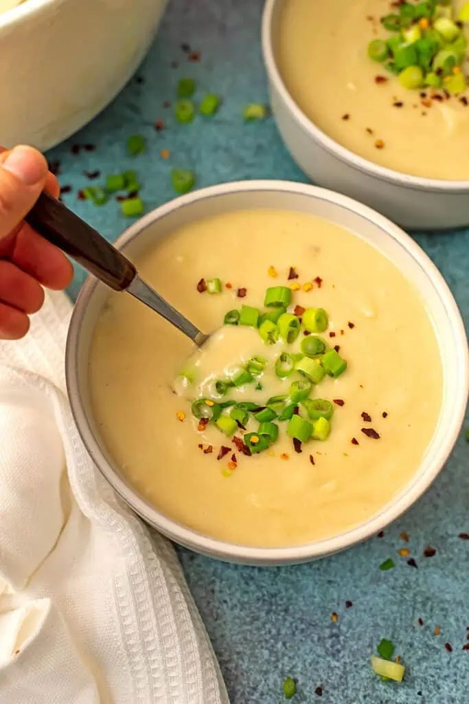 Hand holding a wooden spoon in a bowl of vegan potato soup.