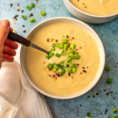 Vegan potato soup in a white bowl with a hand holding a spoon in the soup.