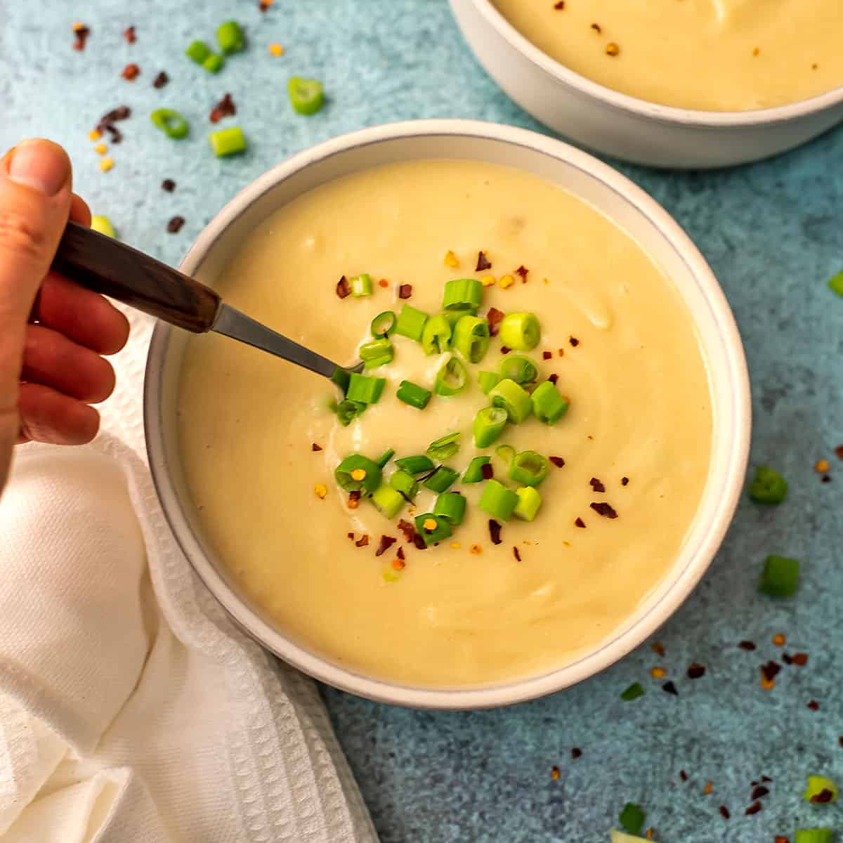 Vegan potato soup in a white bowl with a hand holding a spoon in the soup.