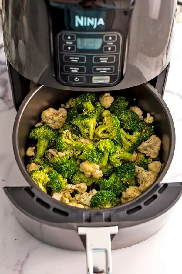 Broccoli and cauliflower in air fryer basket before roasting.