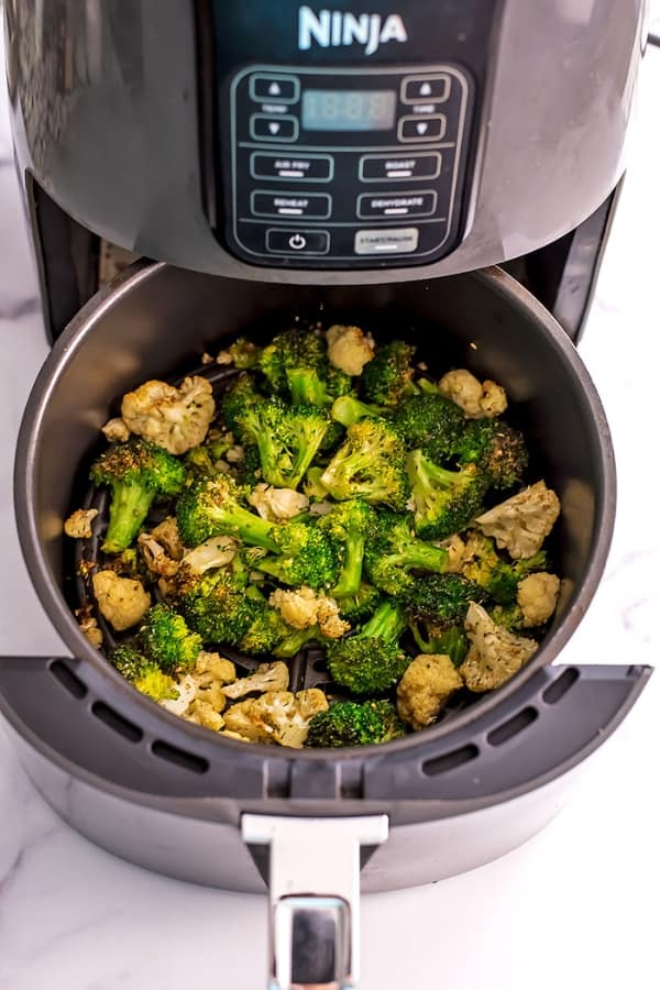 Broccoli and cauliflower in air fryer basket after roasting.