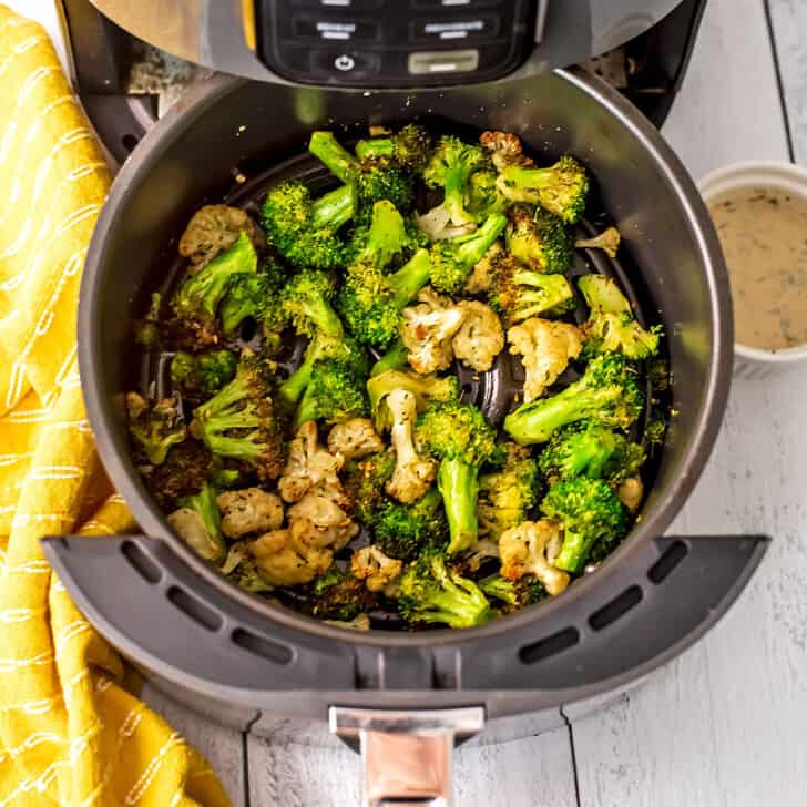 Broccoli and cauliflower in an air fryer basket with yellow napkin.