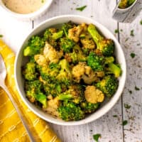 Air fried broccoli and cauliflower in a white bowl with a yellow napkin on the side.