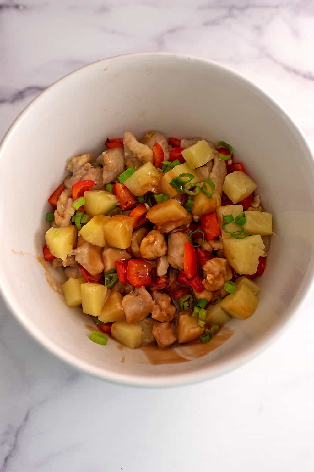 Sweet and sour sauce added to bowl with chicken, pineapple and red bell peppers.