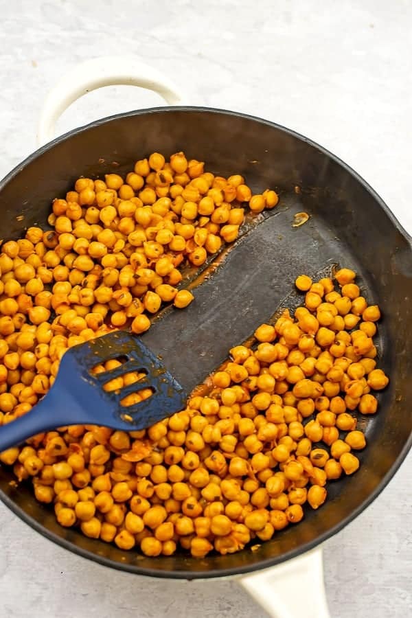 Spatula scraping the middle of a cast iron skillet filled with buffalo chickpeas.