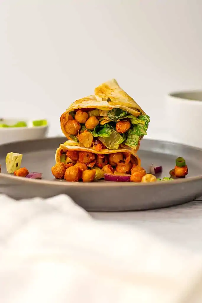 Buffalo chickpea wrap, cut in half, stacked on top of itself on plate.