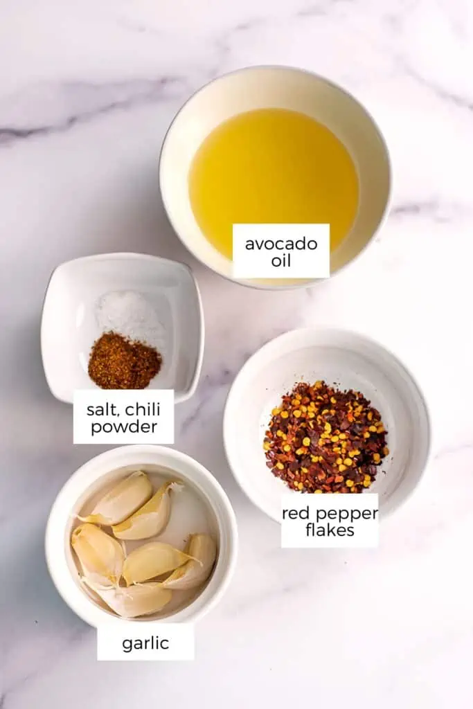 Ingredients to make garlic chili oil in white bowls on a marble countertop.