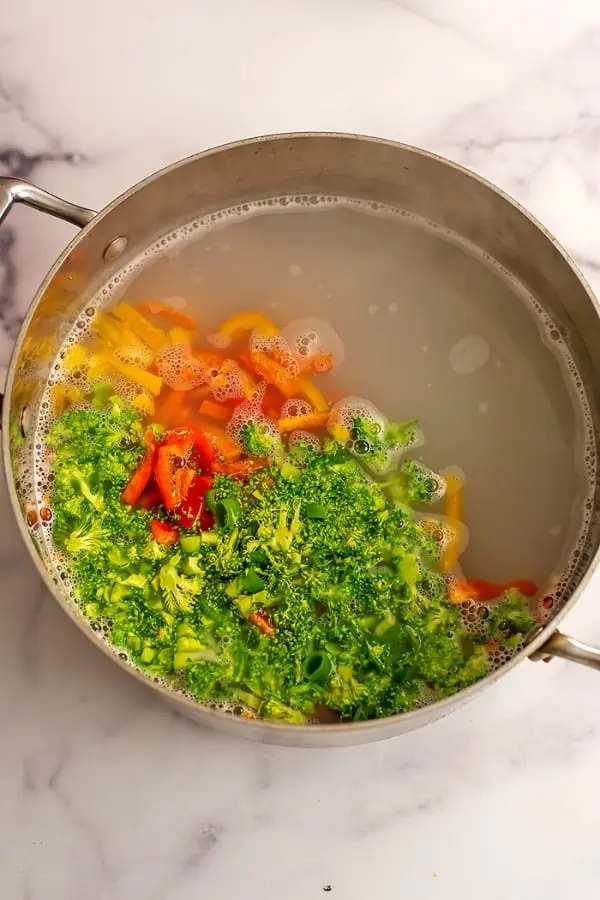 Chopped broccoli and bell peppers added to boiling water.