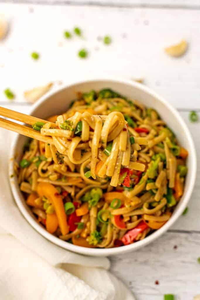 Spicy noodles being picked up by wood chopsticks out of a bowl.