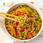 Wood chopsticks picking up spicy noodles out of a white bowl.